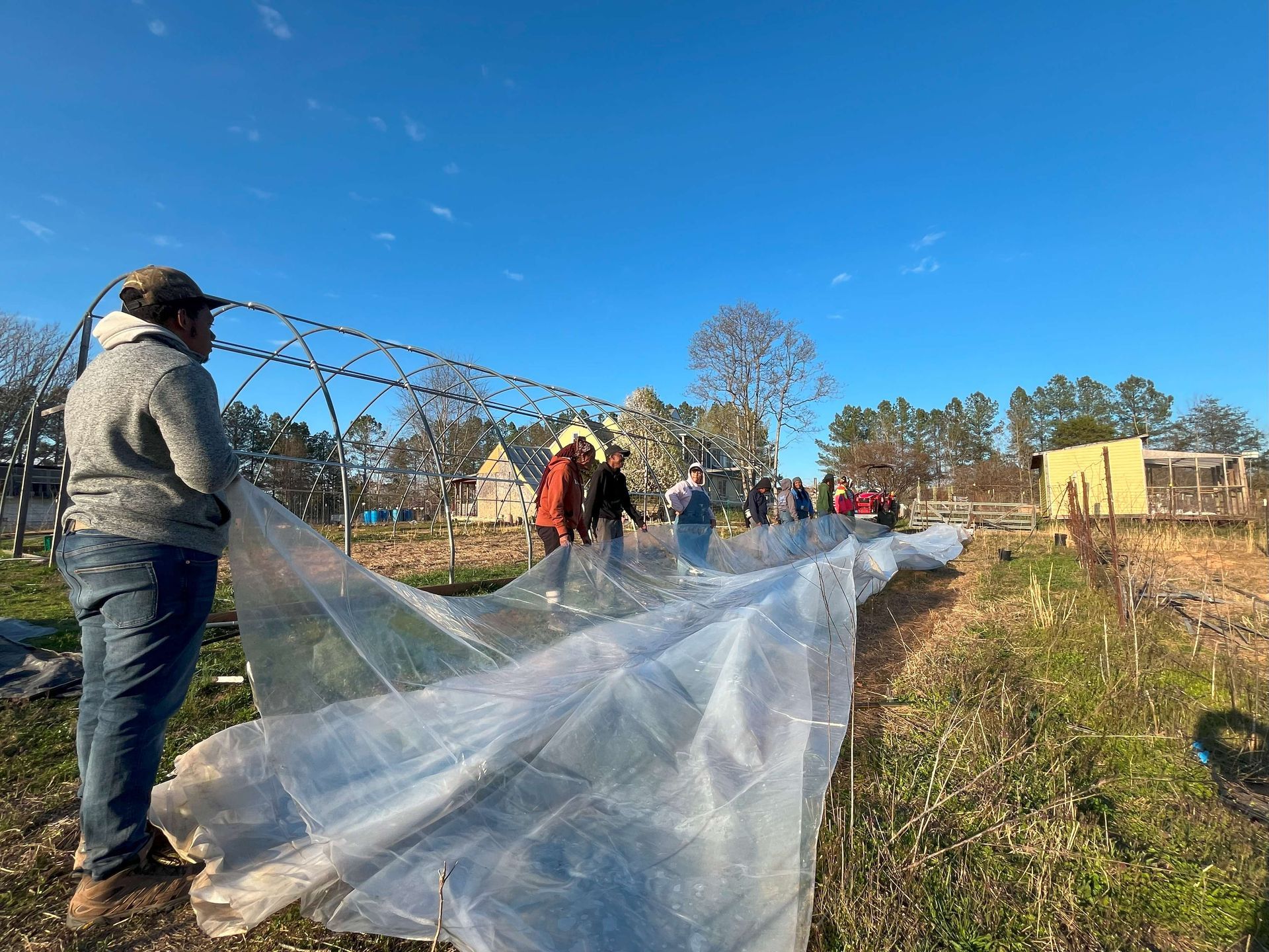 A group of people are working on a greenhouse in a field.