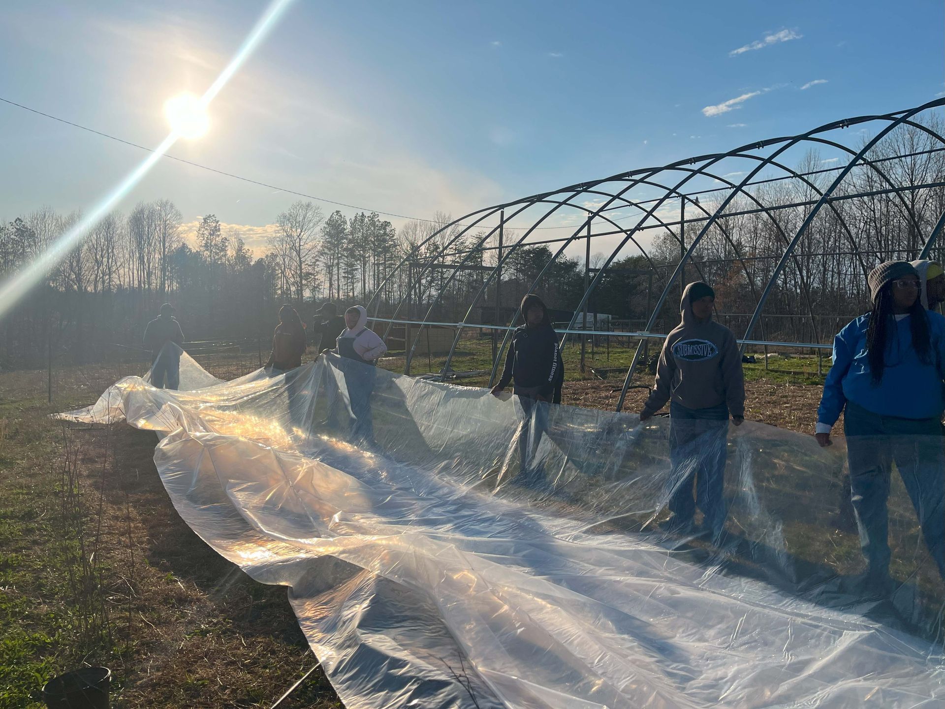A group of people are standing in front of a greenhouse covered in plastic.