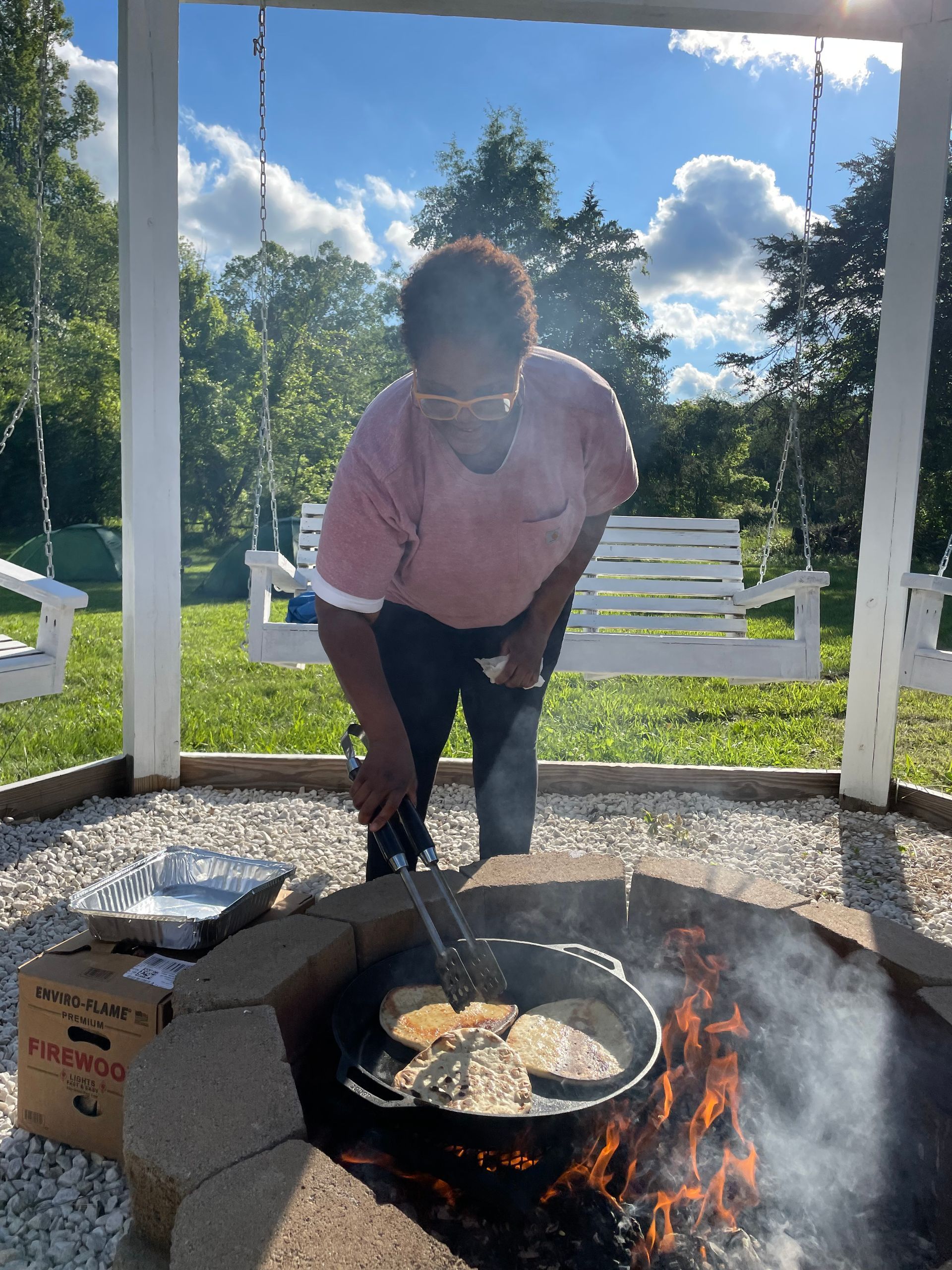 A woman is cooking pancakes over a fire pit