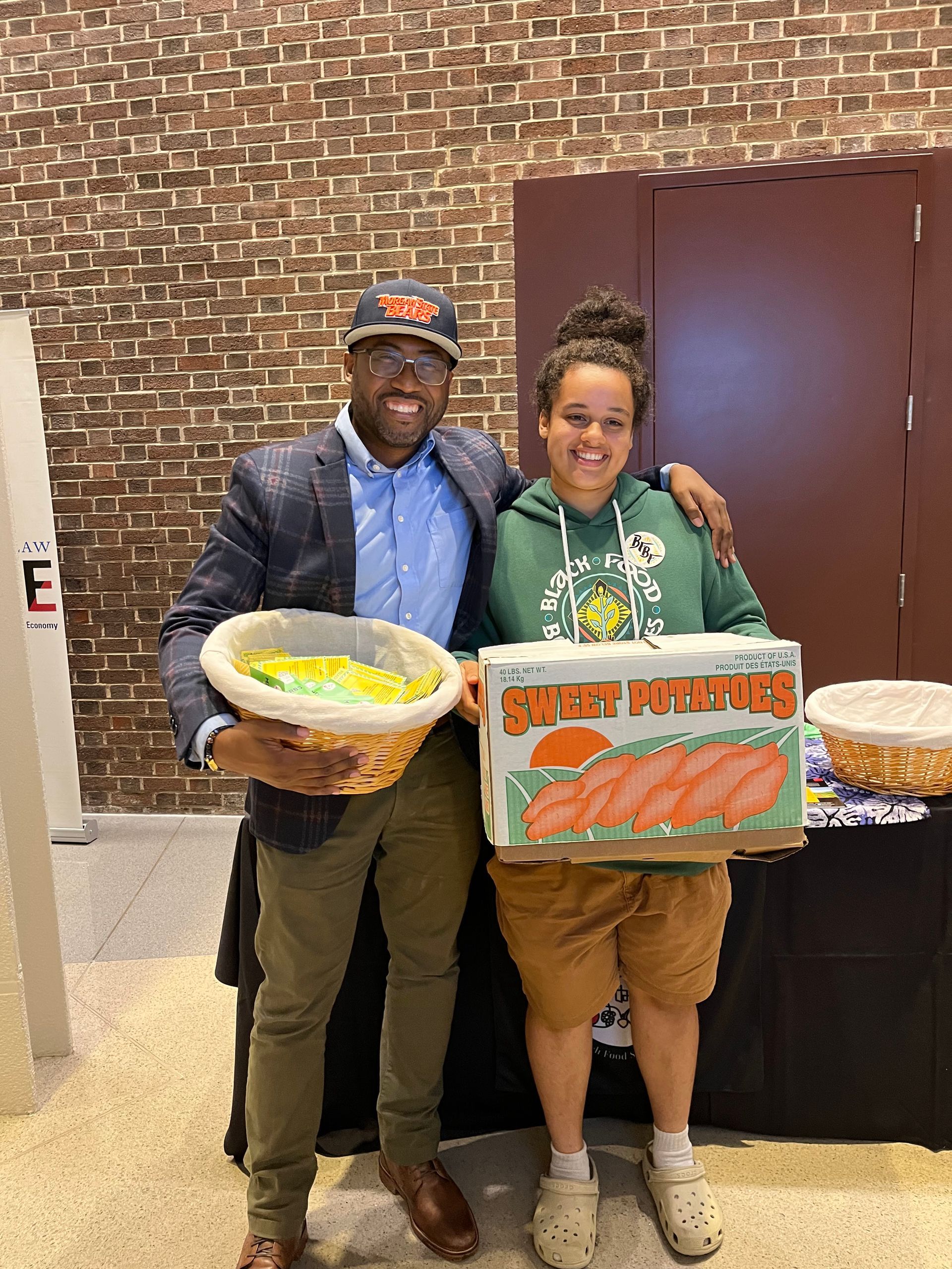 A man and a woman holding baskets and a box of sweet potatoes