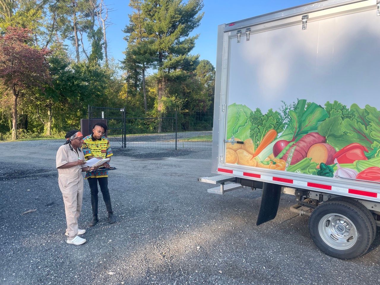Two people are standing in front of a vegetable truck