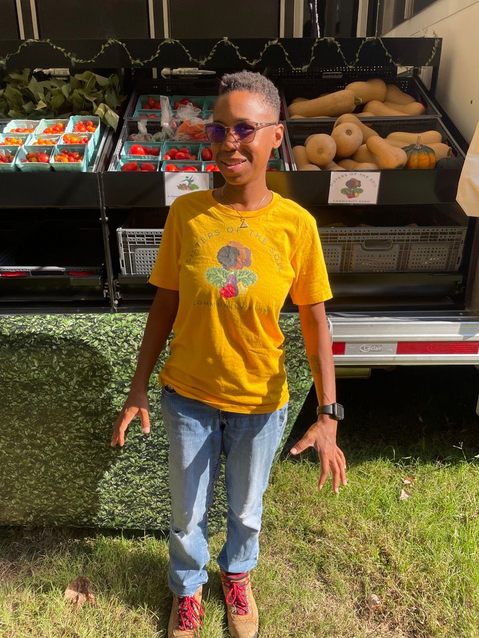 A woman in a yellow shirt is standing in front of a display of fruits and vegetables.