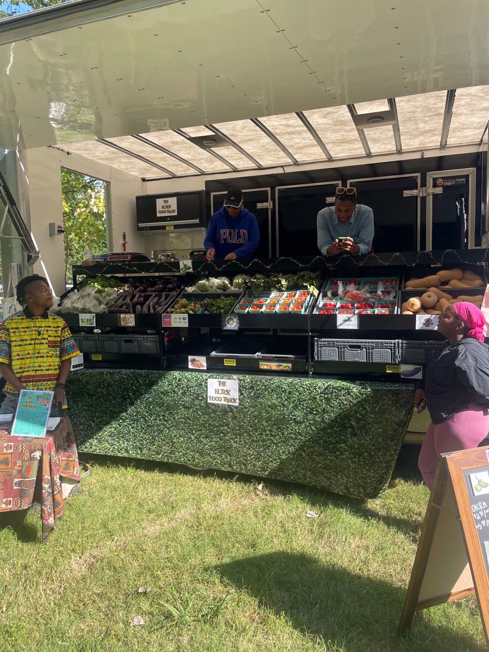 A group of people are standing in front of a food truck selling fruits and vegetables.