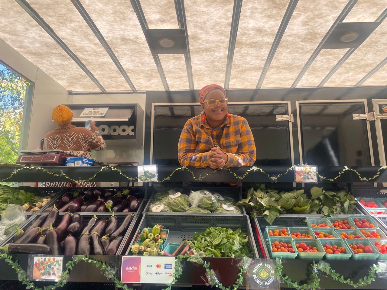 A man in a plaid shirt is standing in front of a display of fruits and vegetables.