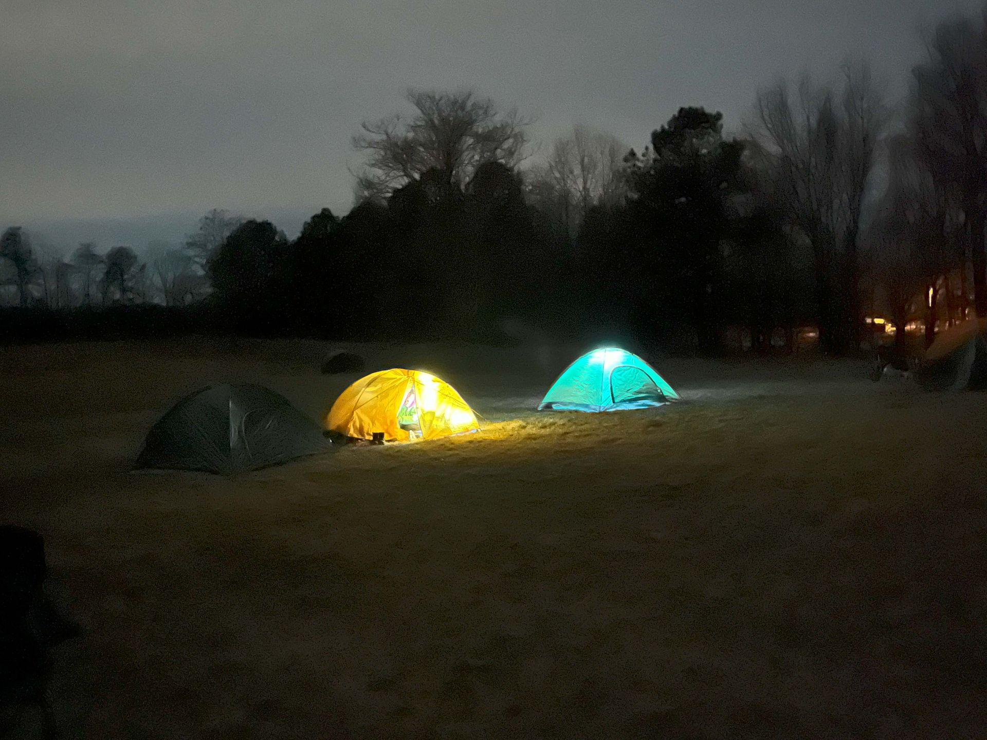 Two tents are lit up in a field at night.