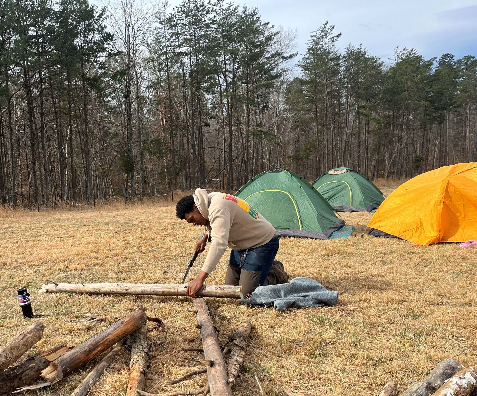 A man is kneeling down in a field with tents in the background.
