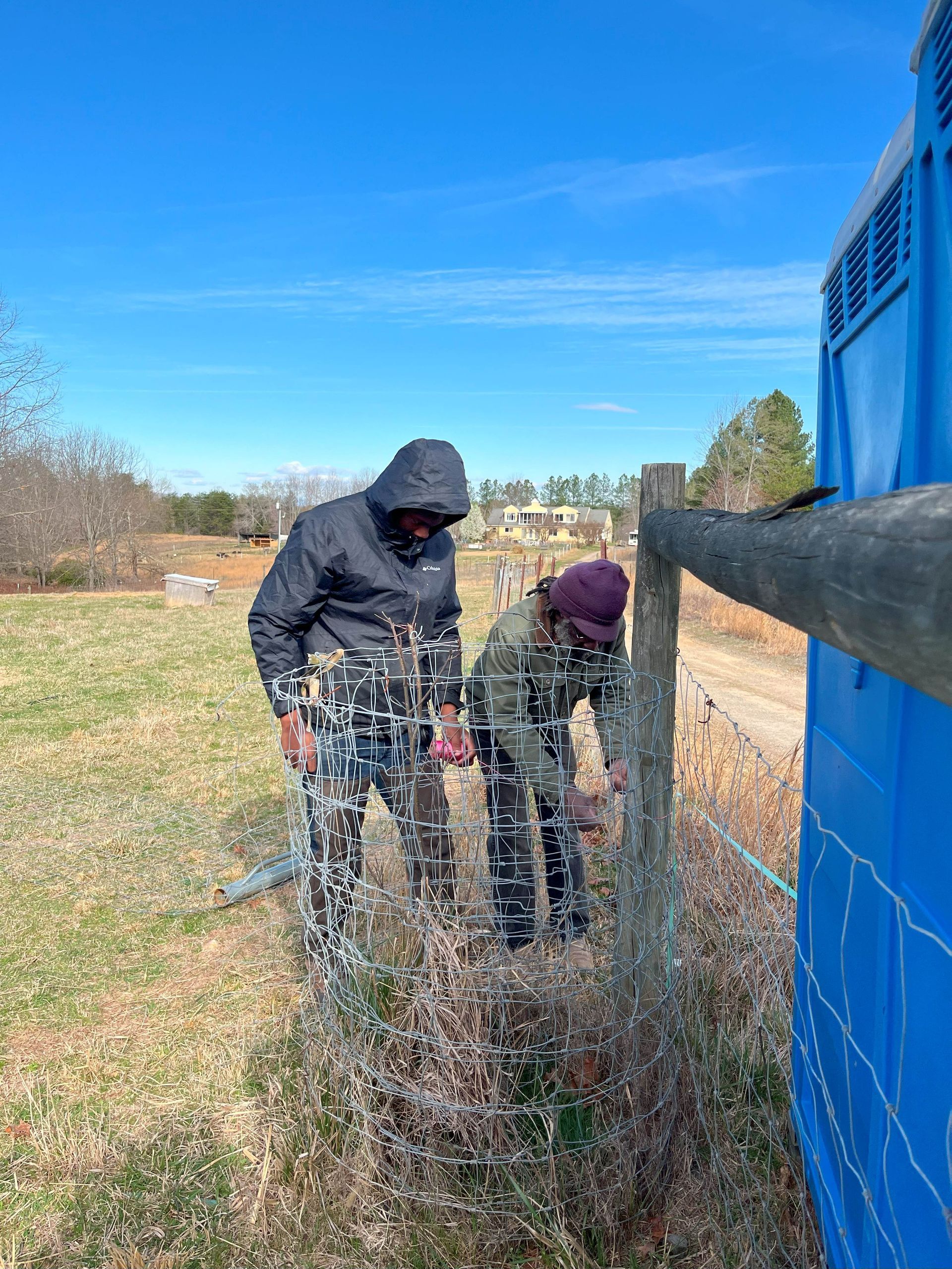 Two people are working on a fence in a field.