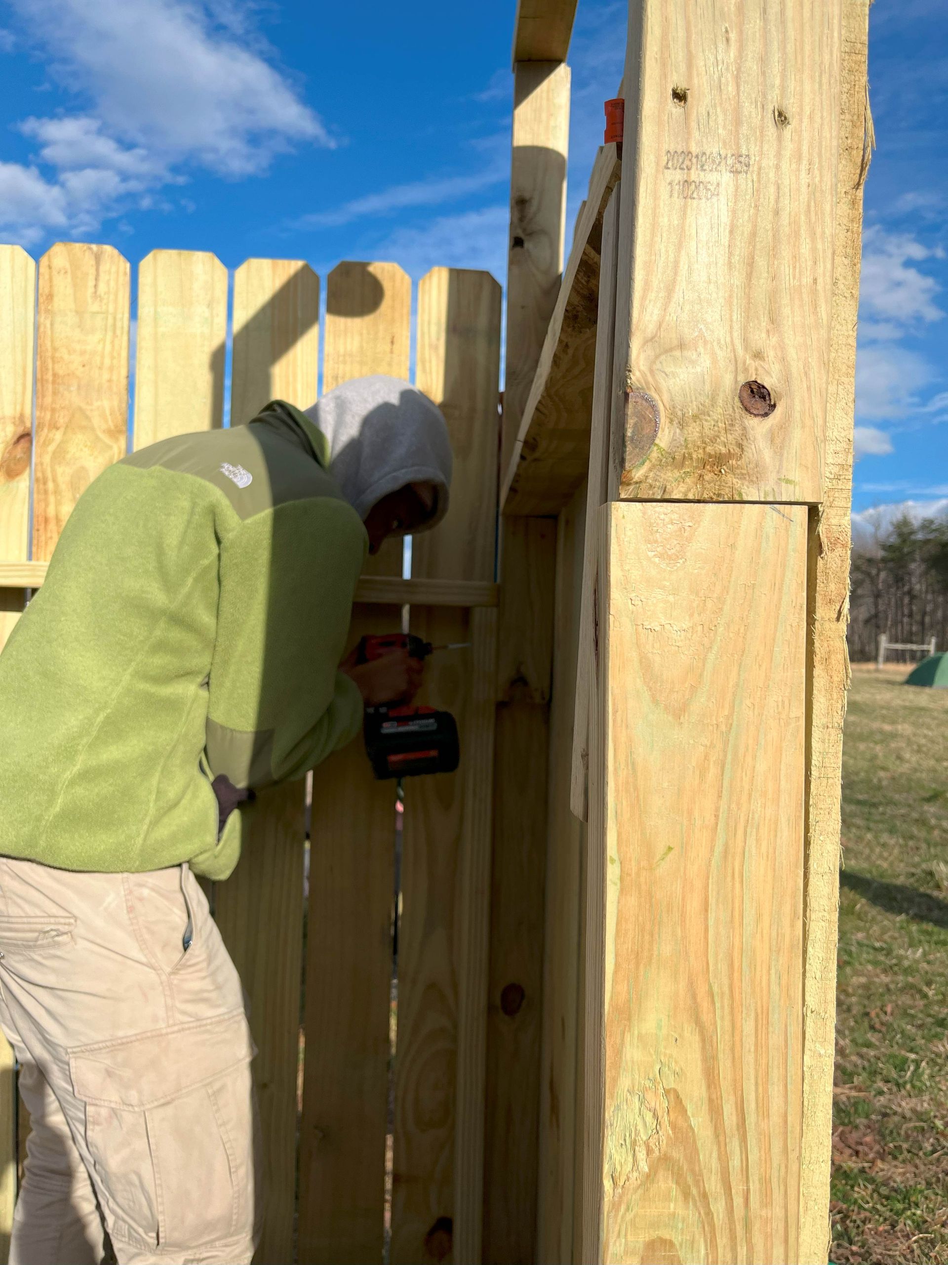 A man in a green jacket is working on a wooden fence