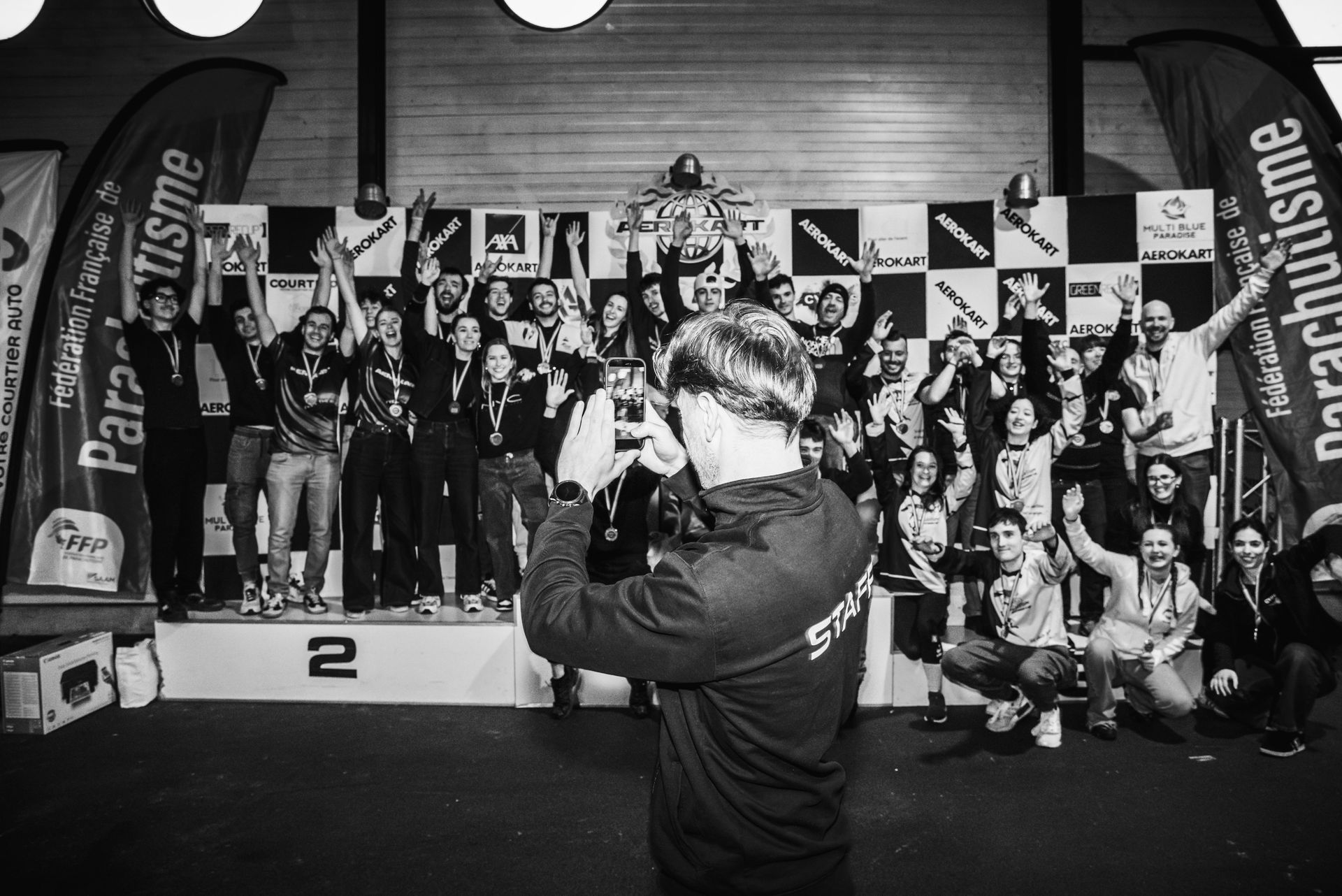 A group of people standing on a podium for a parachuting awards ceremony, with a person in the foreground taking a photo.