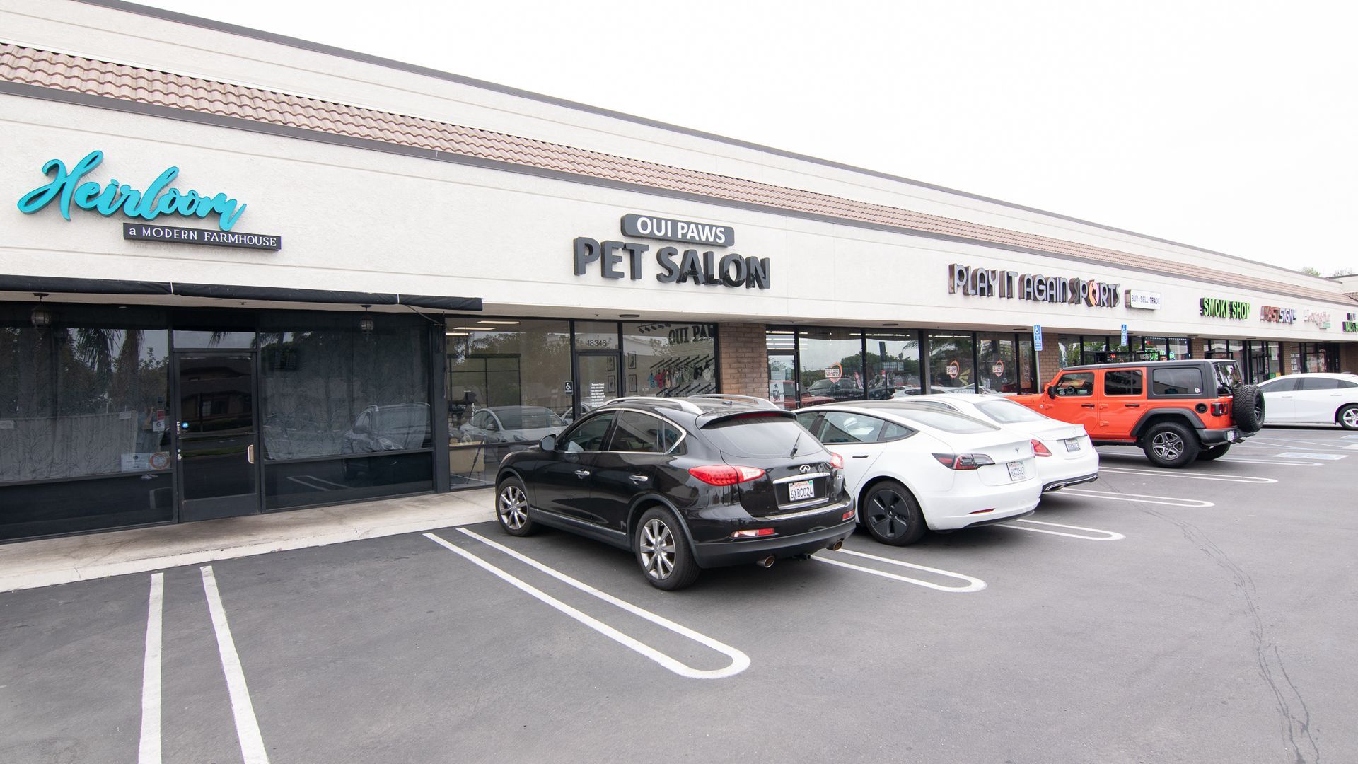 A strip mall with storefronts, including a pet salon, and parked cars.
