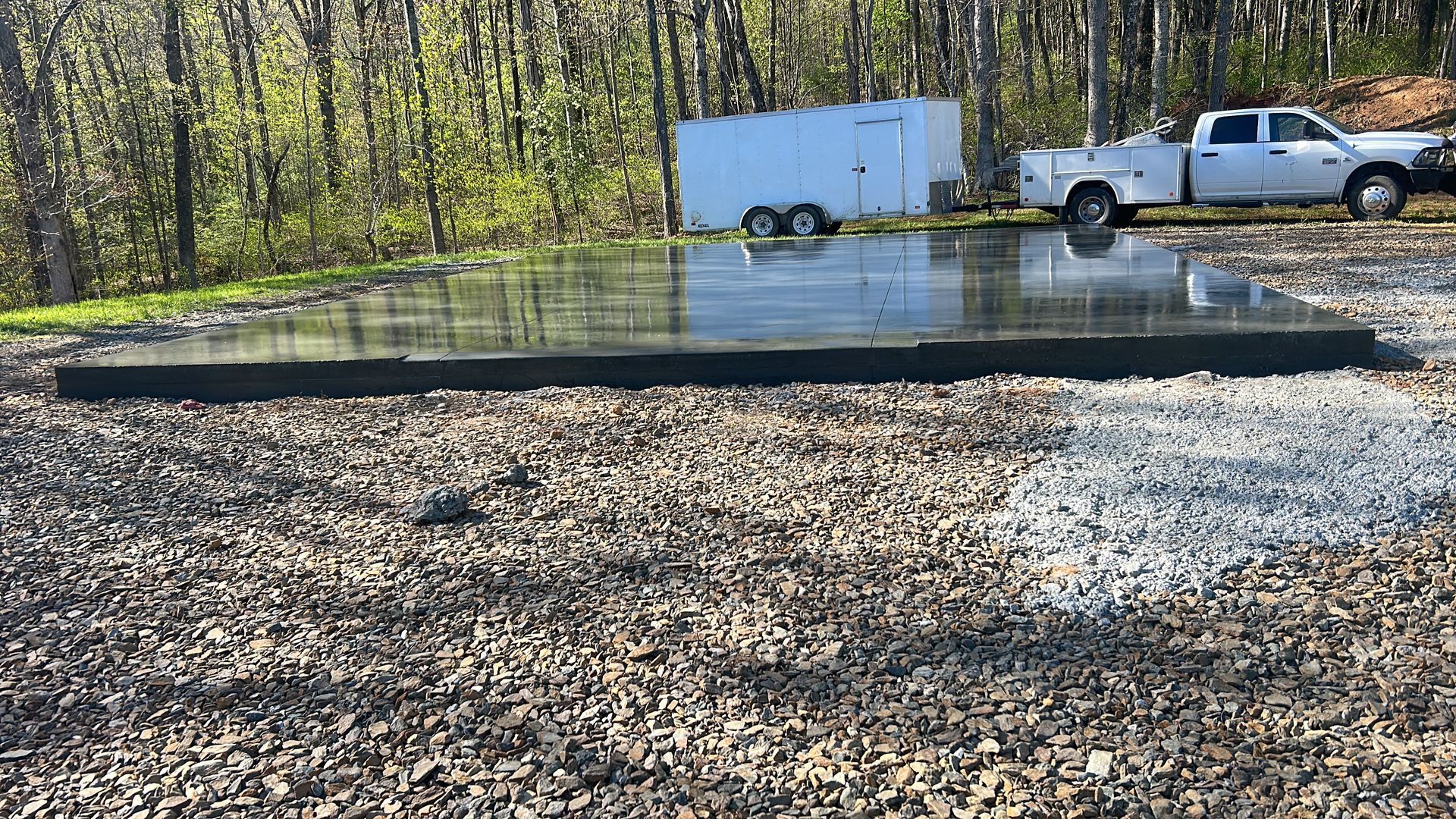 A small black pond liner in a gravel yard with a white truck and trailer parked nearby.