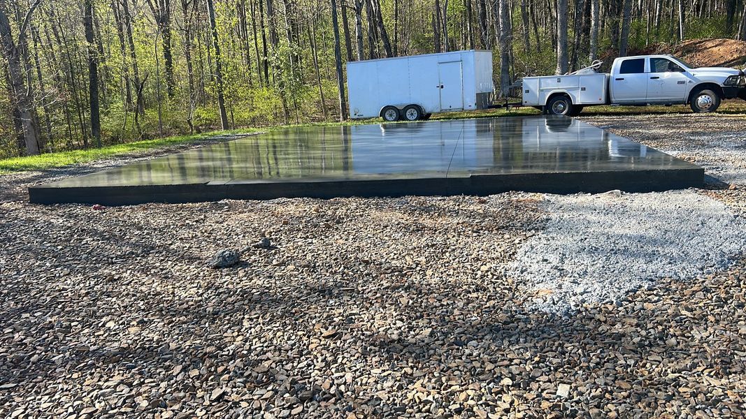 A small black pond liner in a gravel yard with a white truck and trailer parked nearby.