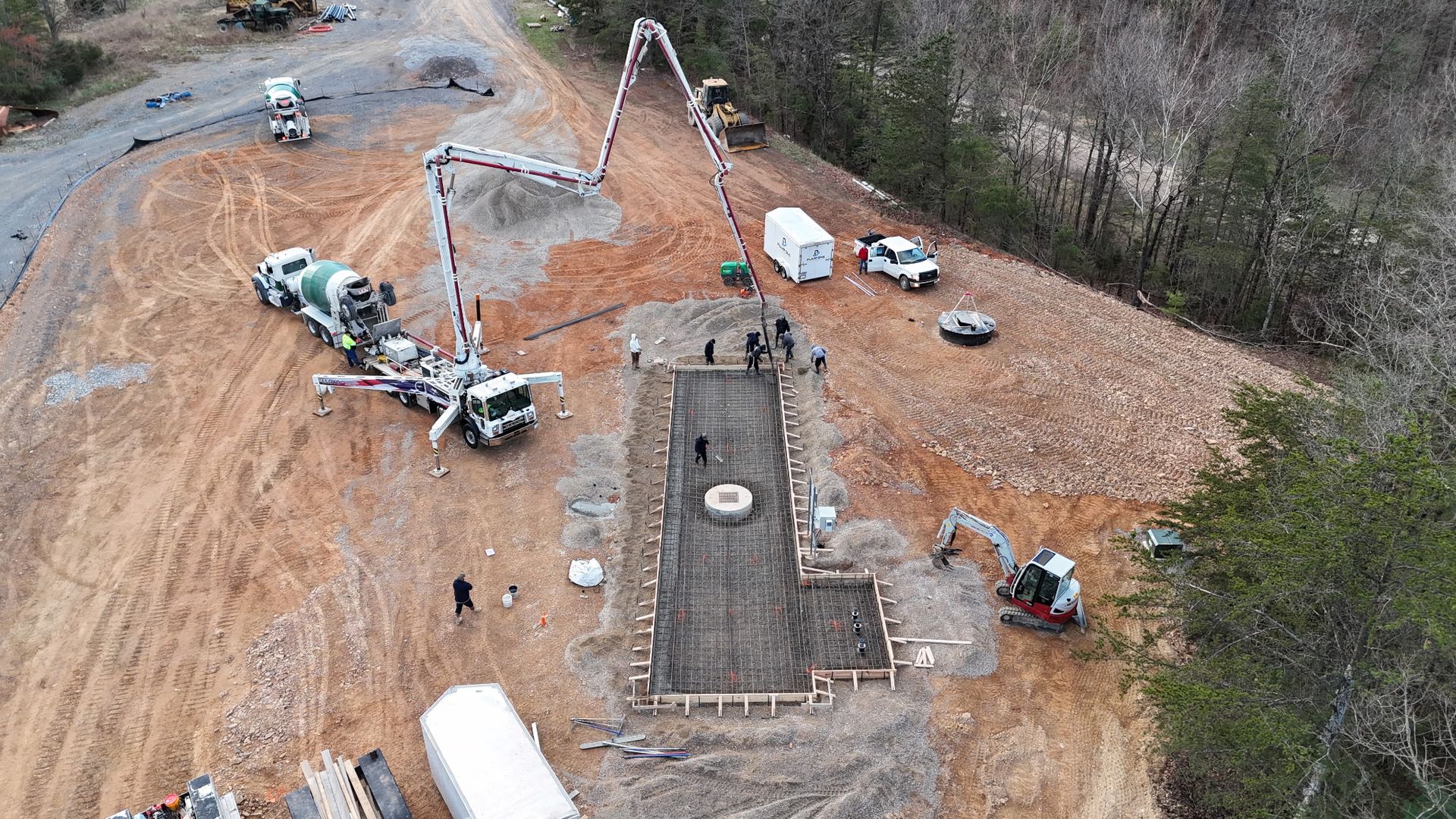 Aerial view of a construction site with a large concrete foundation, crane truck, and scattered equipment on bare ground