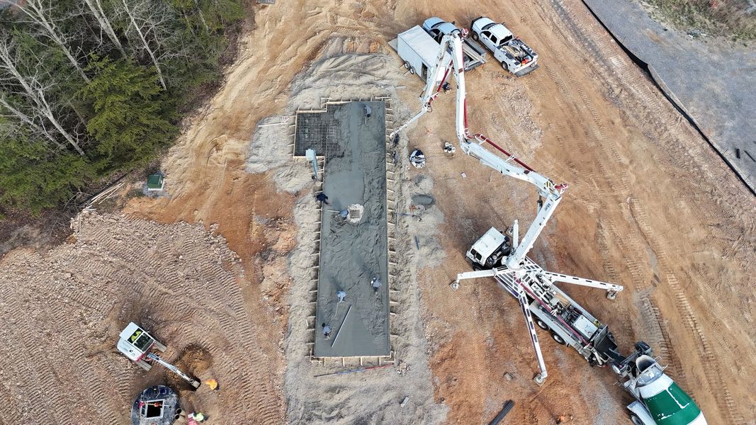Aerial view of a construction site with excavators, trucks, and a long concrete foundation being built.
