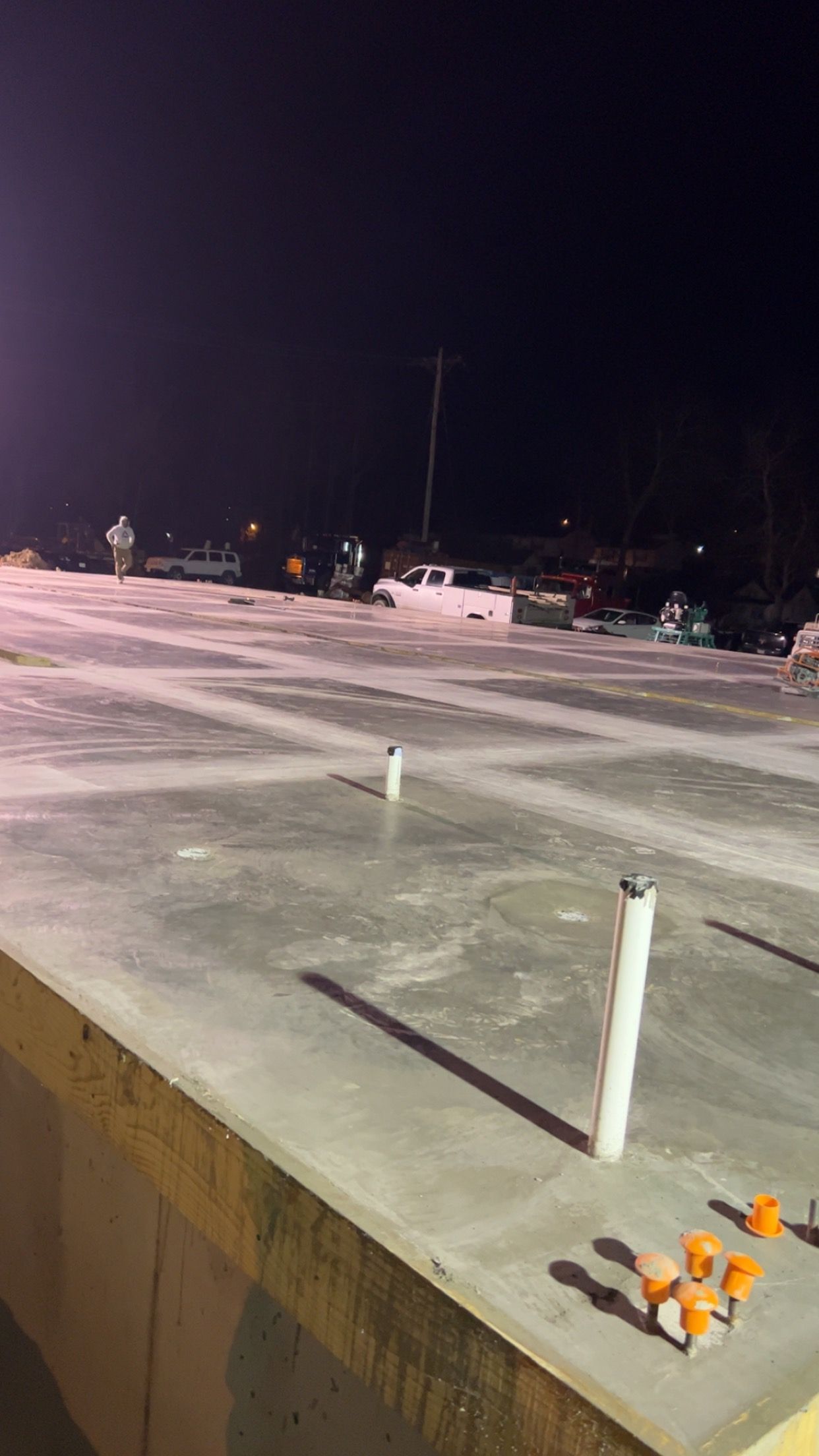 Nighttime parking lot with cars in the distance and a concrete curb in the foreground.