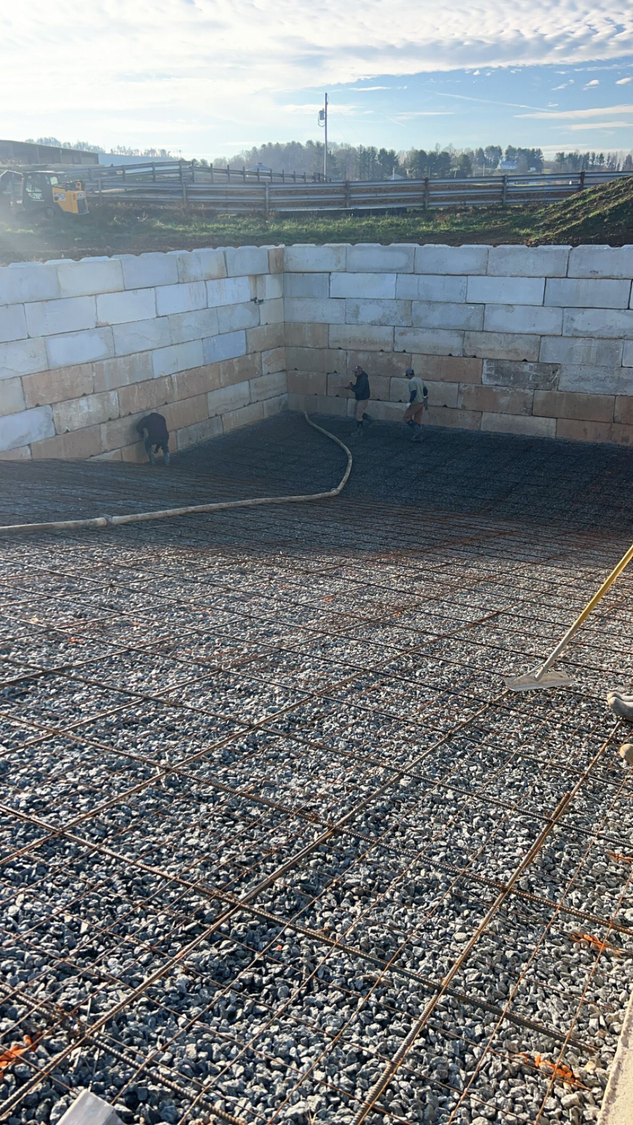 Stone retaining wall beside a gravel yard, with a distant skyline under a clear sky.