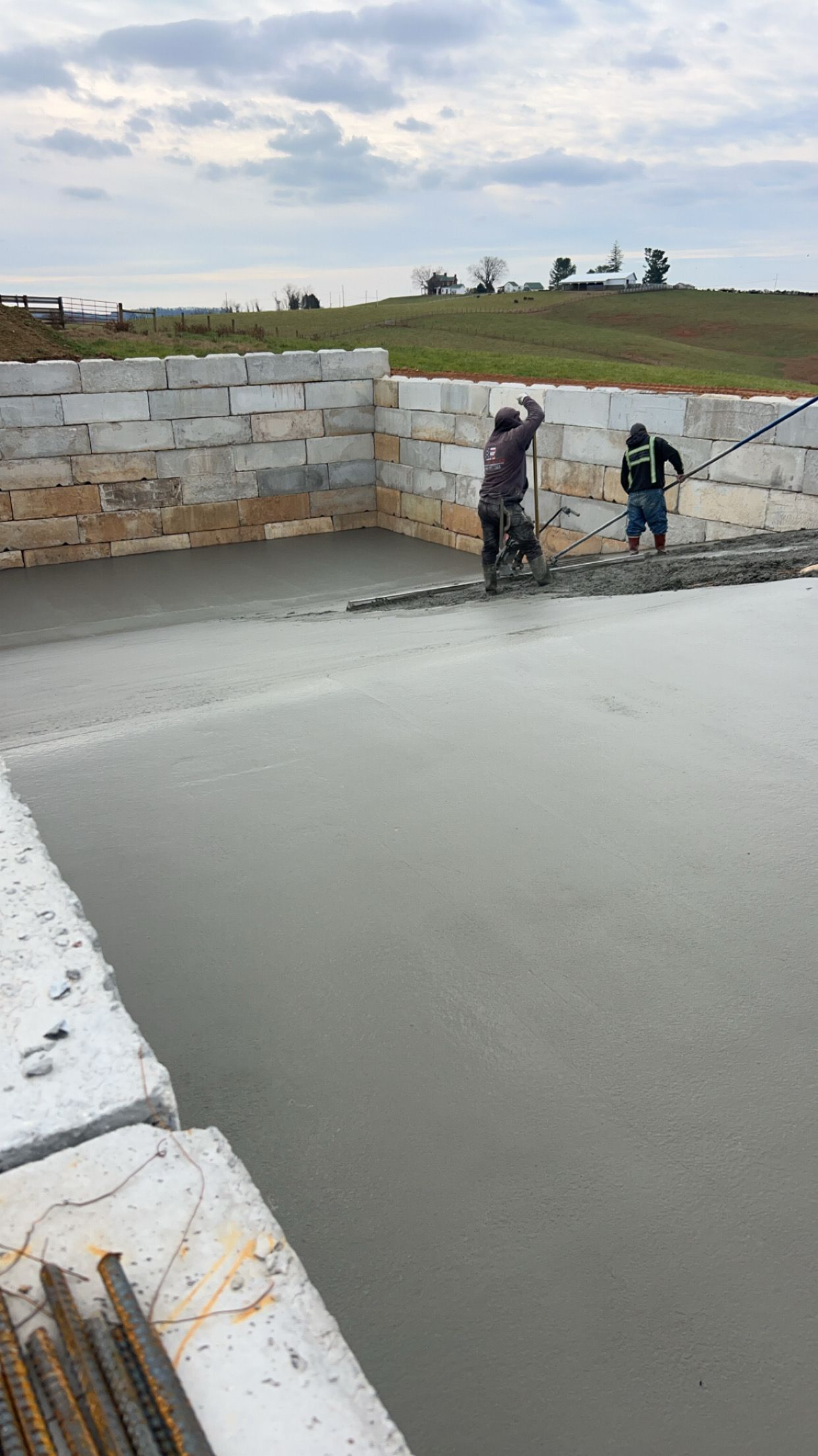 Workers smoothing wet concrete near a stone wall on a construction site outdoors