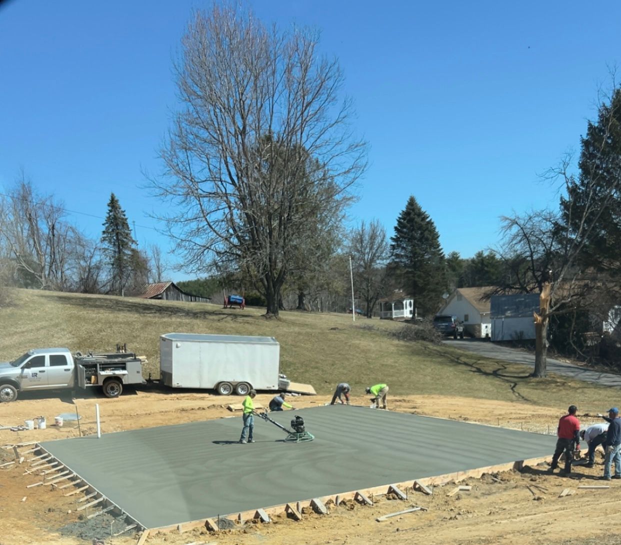 Workers smoothing concrete on a foundation slab at a construction site on a sunny day