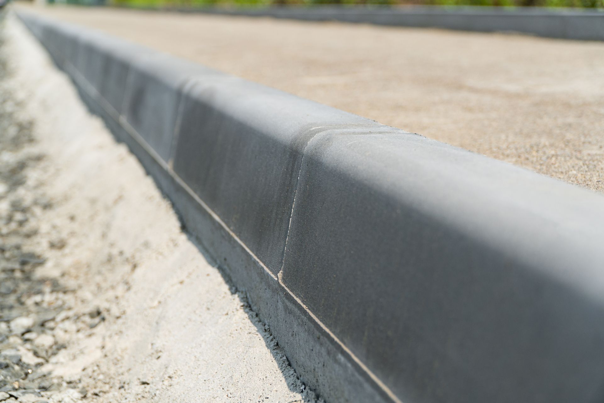 Close-up of a gray concrete curb edging a sandy roadway or sidewalk