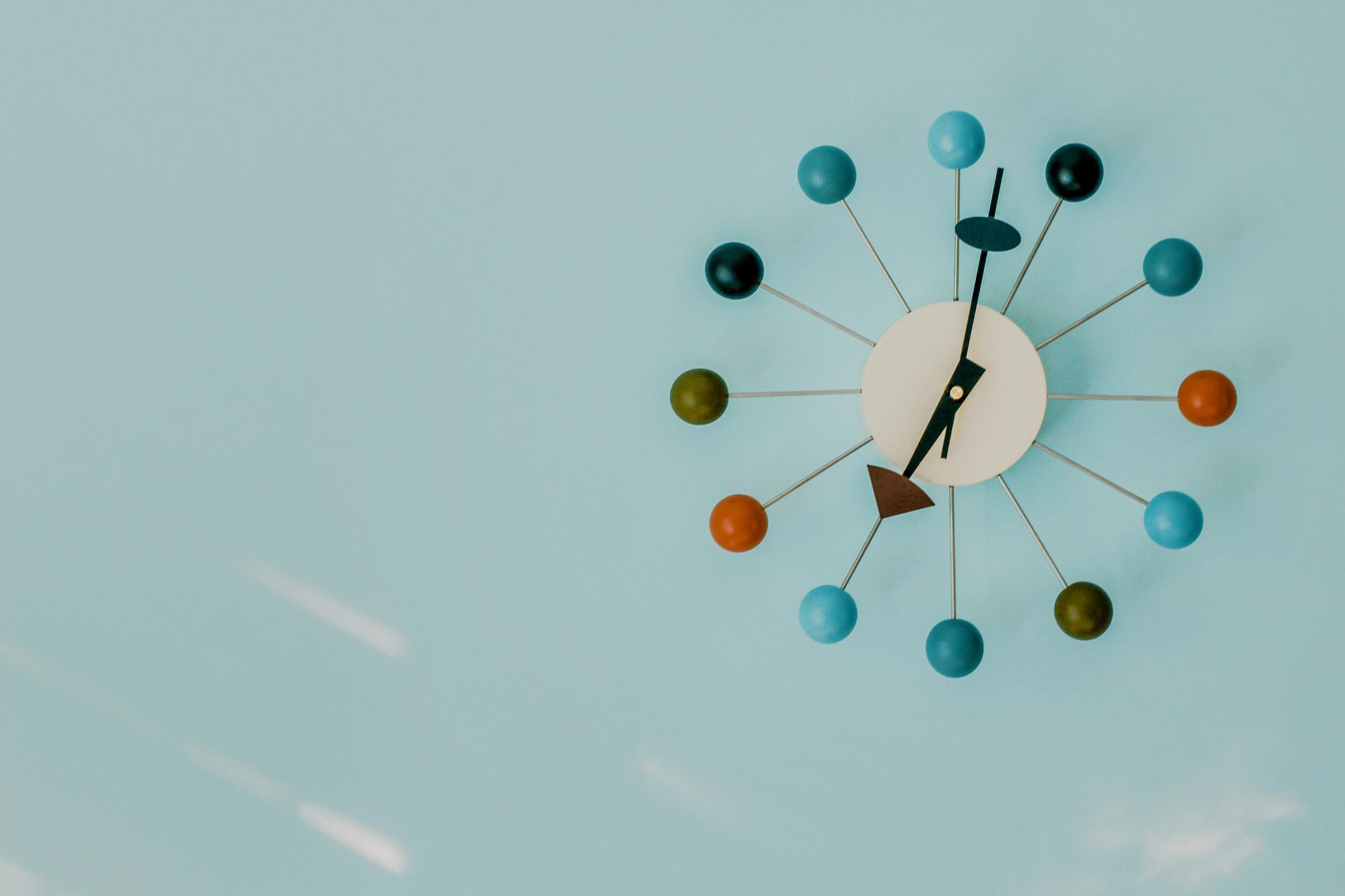 A colorful clock is hanging on a blue wall.