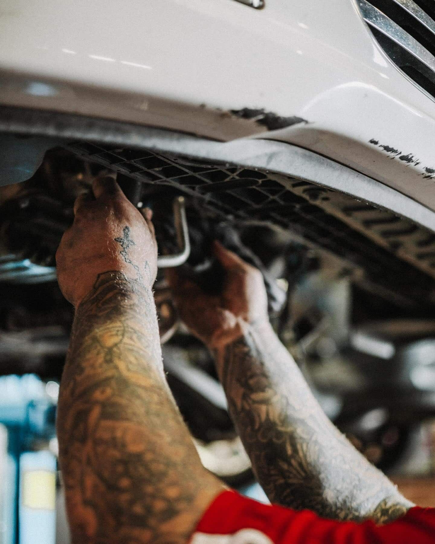 A Man With Tattoos is Working on the Underside of a Car — Nationwide Auto Service Centre in West Gosford, NSW