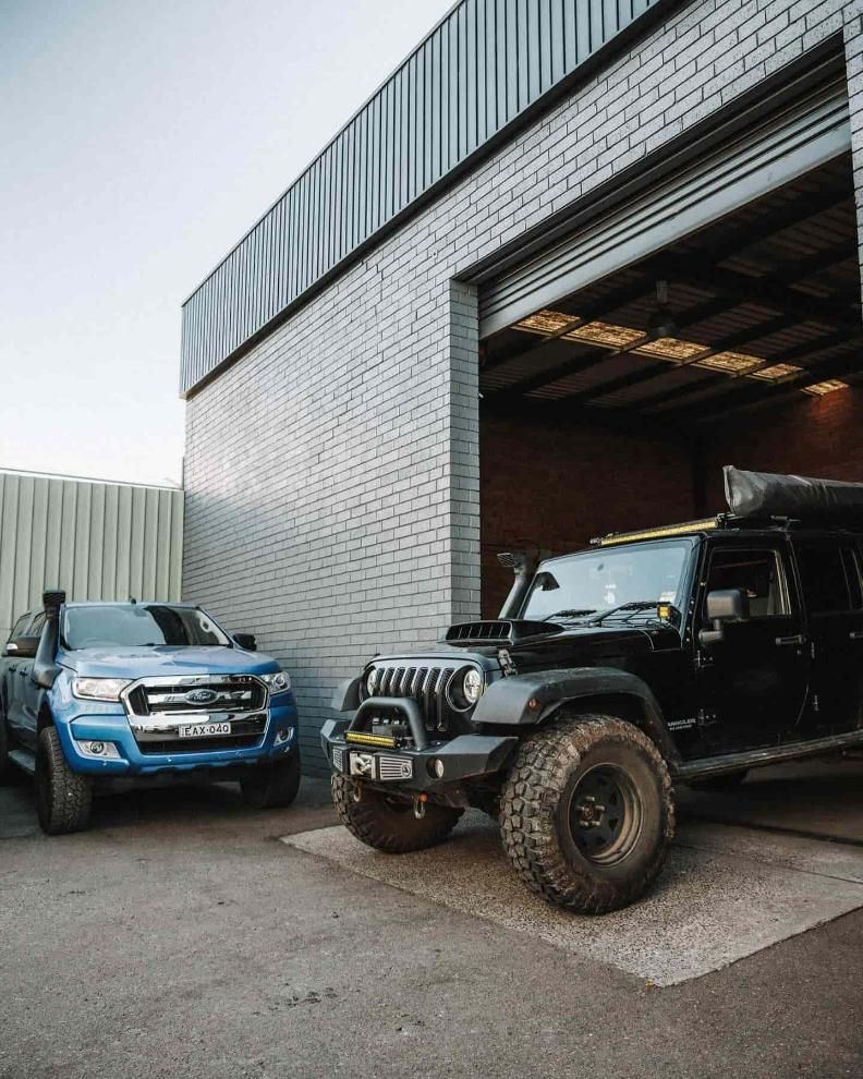 Two 4x4s Are Parked in Front of a Garage Door — Nationwide Auto Service Centre in West Gosford, NSW