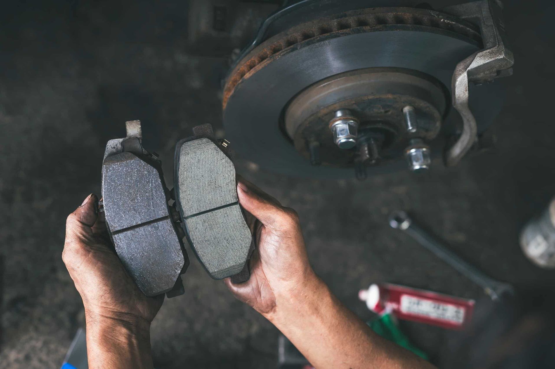 A Person is Holding a Pair of Brake Pads in Front of a Car — Nationwide Auto Service Centre in West Gosford, NSW