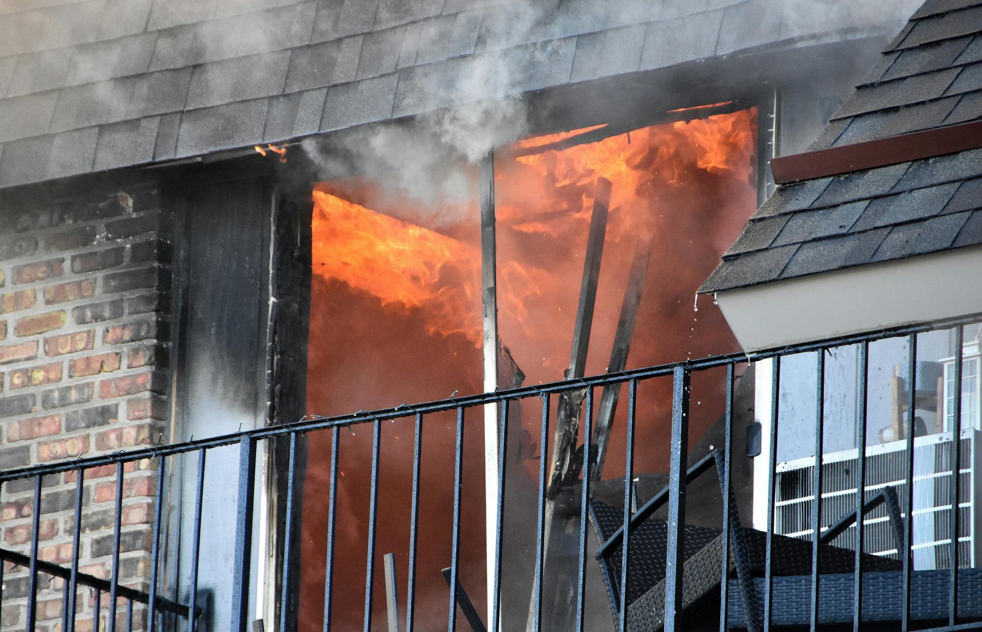 Apartment doorway engulfed in flames, with smoke pouring out past a black metal railing