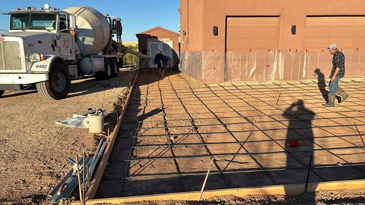 Concrete being poured for a driveway, with truck, prepared rebar grid, worker, and a house in the background.