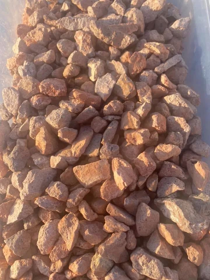 Pile of reddish-brown rocks, likely gravel or decorative stones, outdoors.