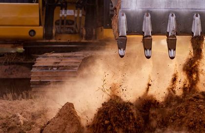 A yellow excavator digging dirt, kicking up dust.