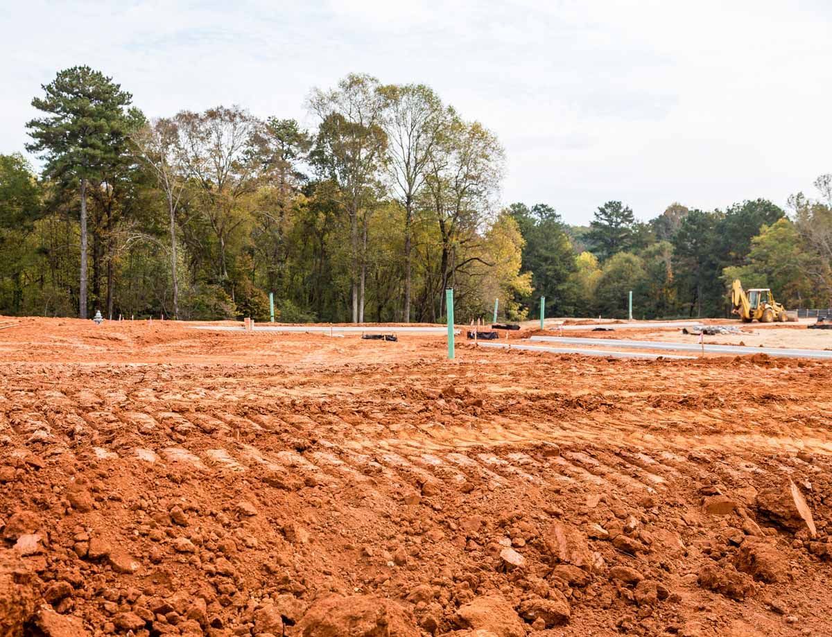 Construction site with red dirt, trees in the background, and a yellow bulldozer.