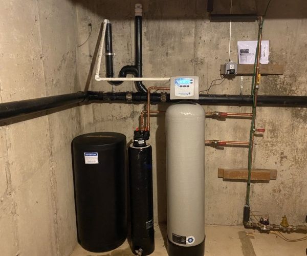Water softener system installed in a basement, consisting of three cylindrical tanks and connected piping.