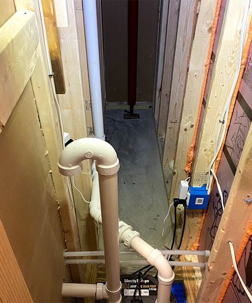 Narrow unfinished basement hallway with plumbing and electrical fixtures.