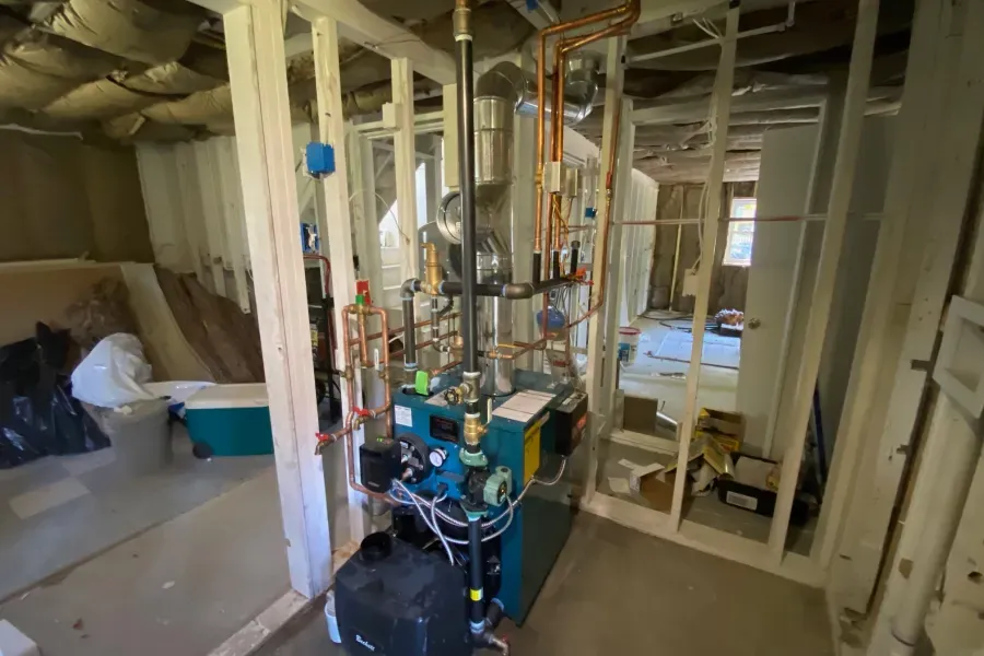 Basement with unfinished framing around a blue boiler and pipes.