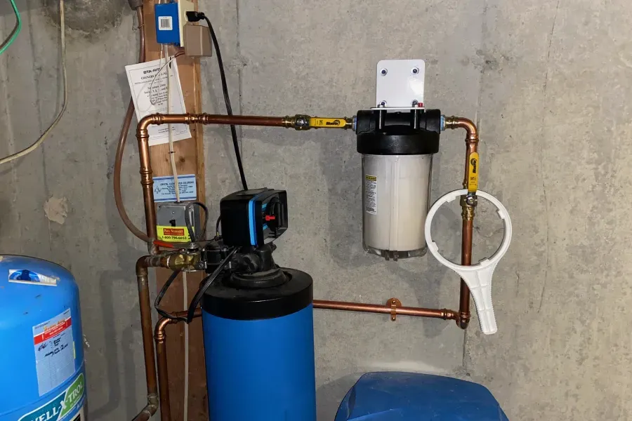 Water filtration system installed on a concrete wall. Copper pipes, blue tank, and white filter housing.