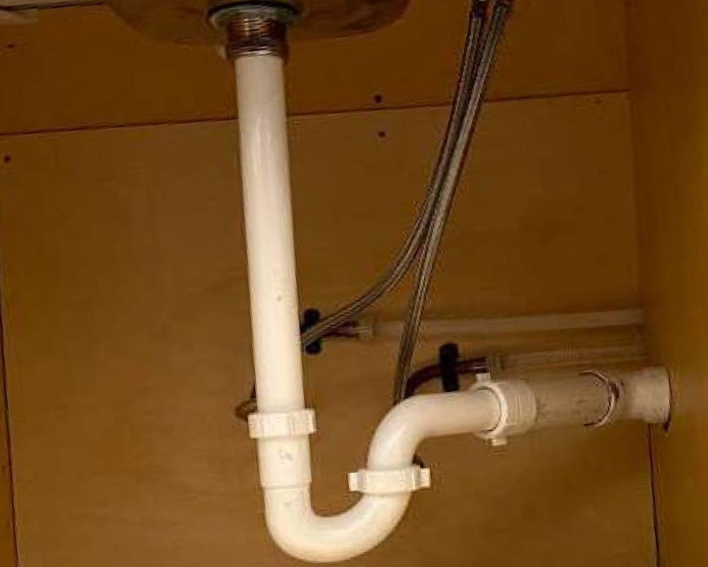 White plastic P-trap plumbing under a kitchen sink.
