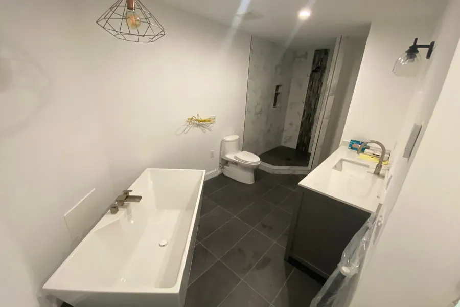 Modern bathroom with white tub, toilet, and sink, dark gray tiled floor, and shower.