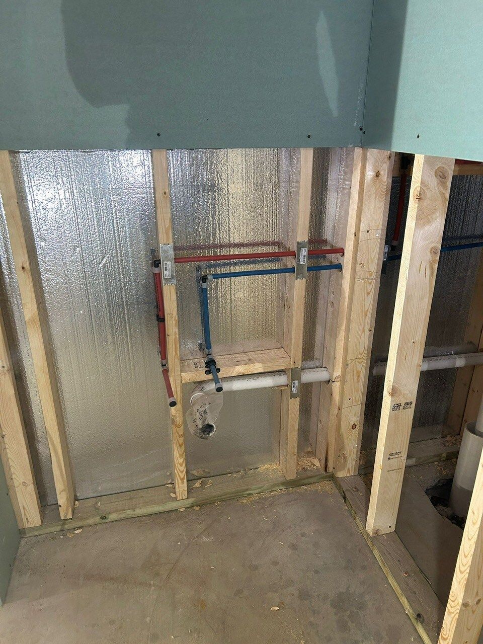 Framed bathroom wall with plumbing pipes, insulated silver foil, and unfinished drywall.