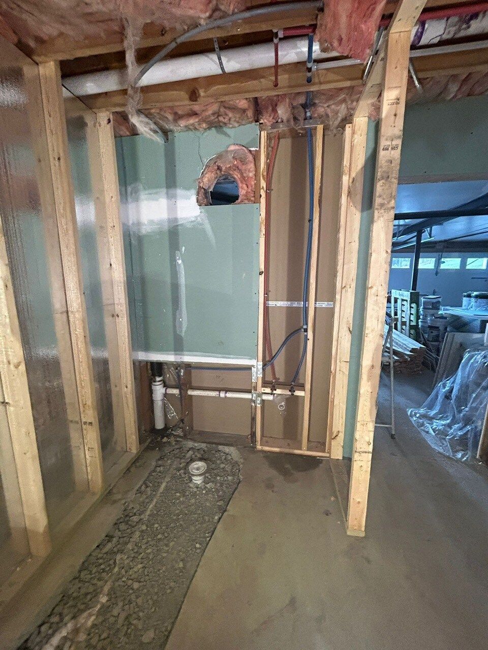 Framed wall with plumbing and cement flooring, likely a construction site.