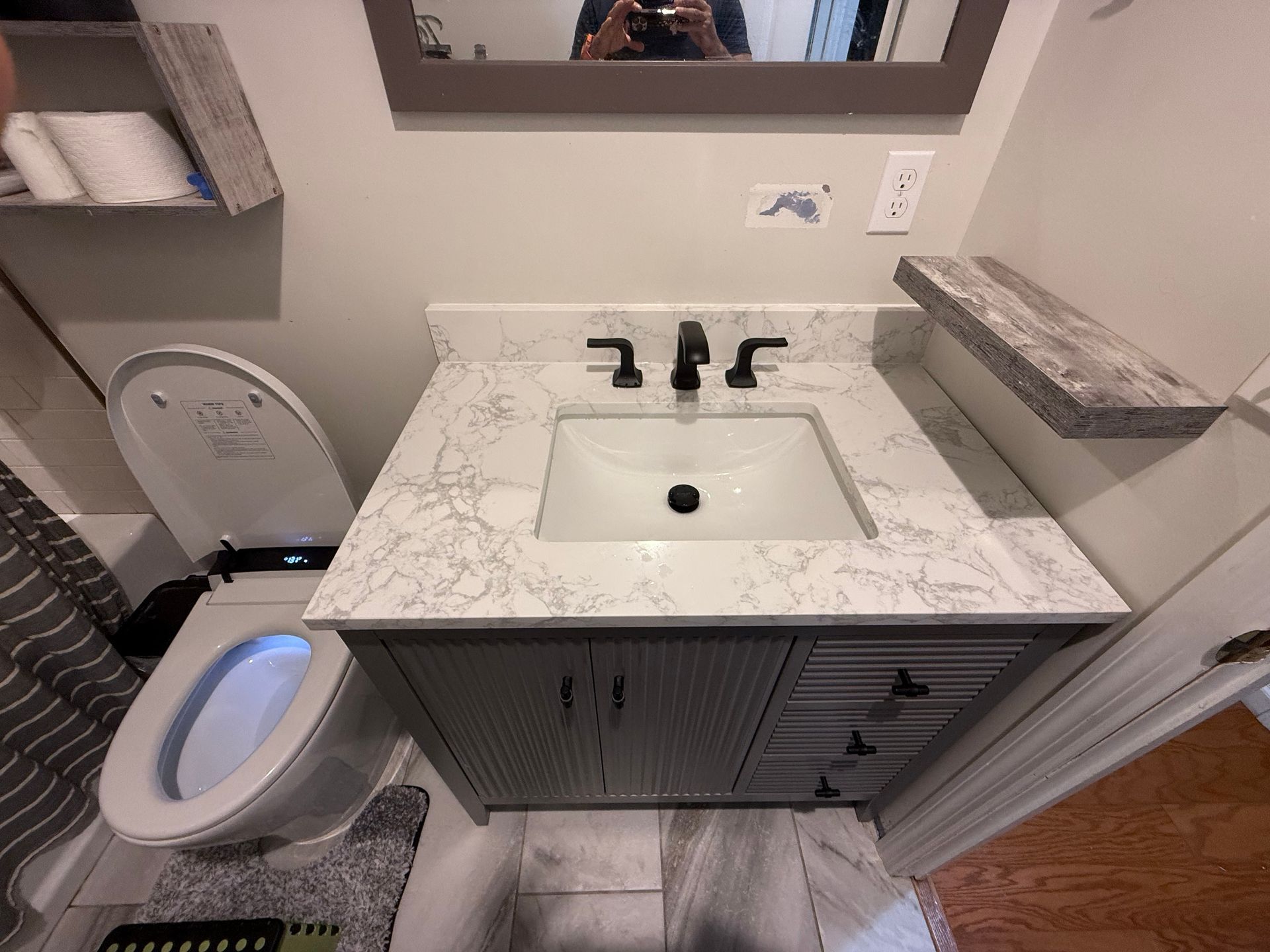 Bathroom with gray vanity, marble countertop, black faucet, and smart toilet.