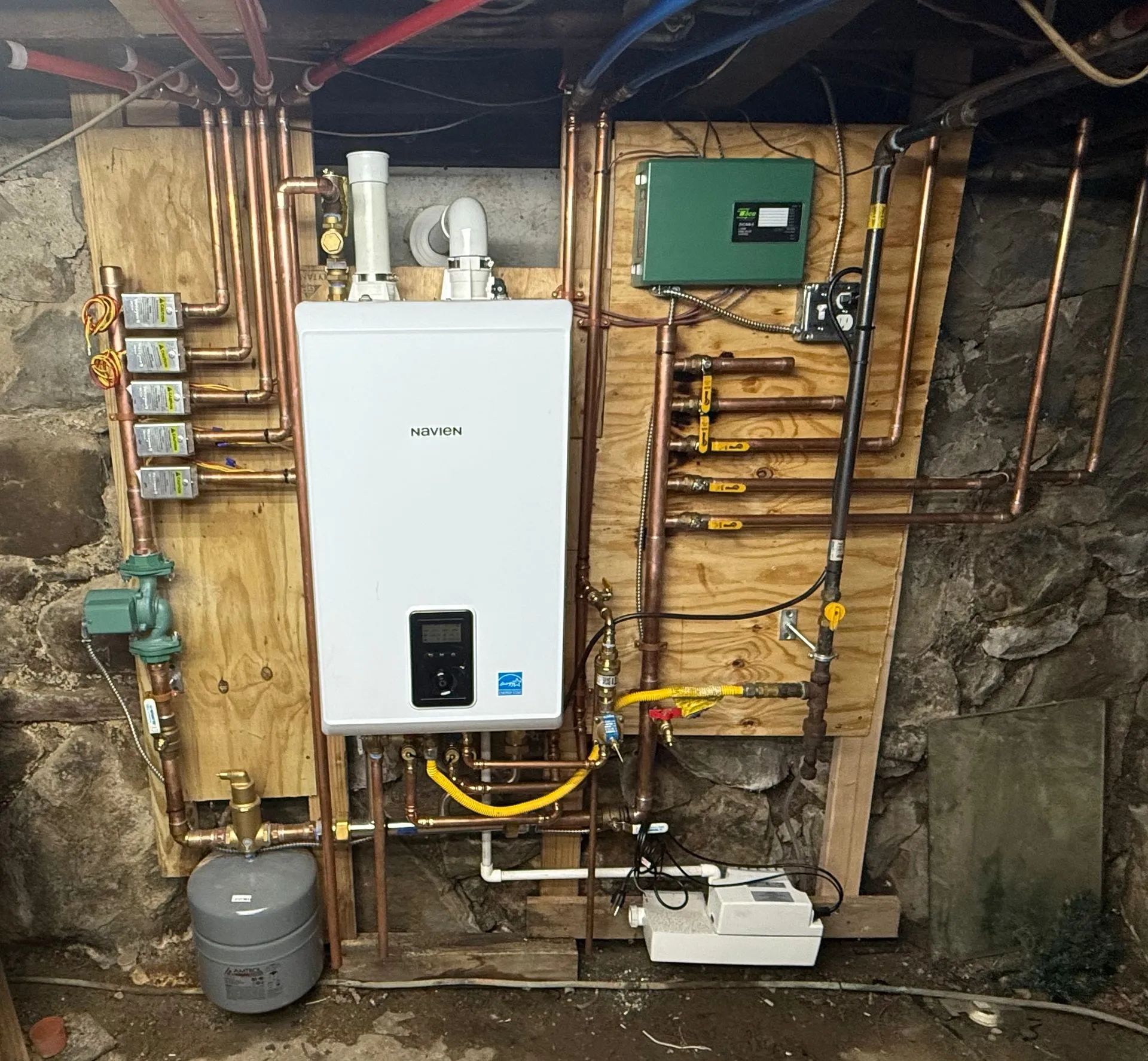 Gas boiler and plumbing against a stone wall; copper pipes, electrical boxes, and a control panel.