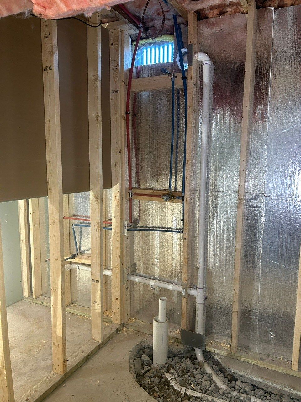 Framing of a wall in a basement, with exposed pipes and plumbing.