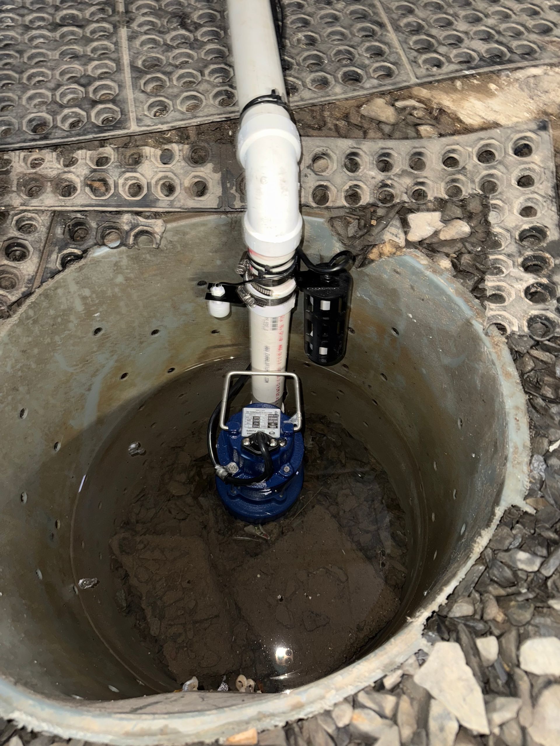 Sump pump in a concrete basin, with a white PVC pipe and a black electrical component attached.
