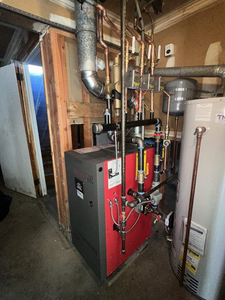 Red and gray boiler with copper pipes in a utility room.  A water heater is adjacent.
