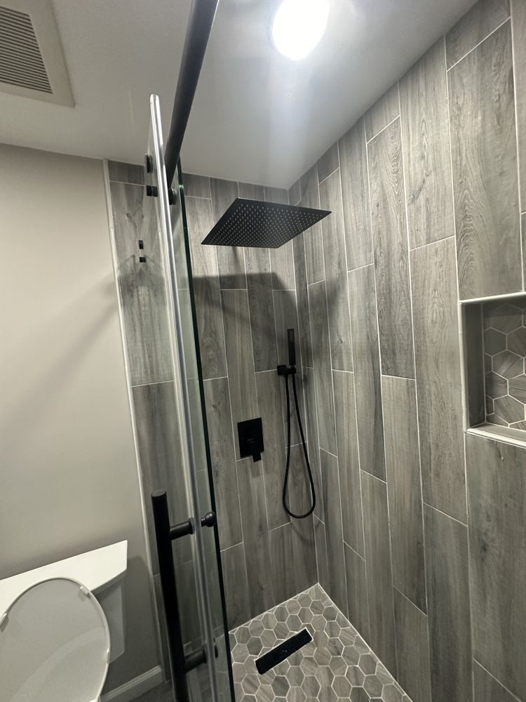 Modern shower with gray tiled walls, black fixtures, and glass door.