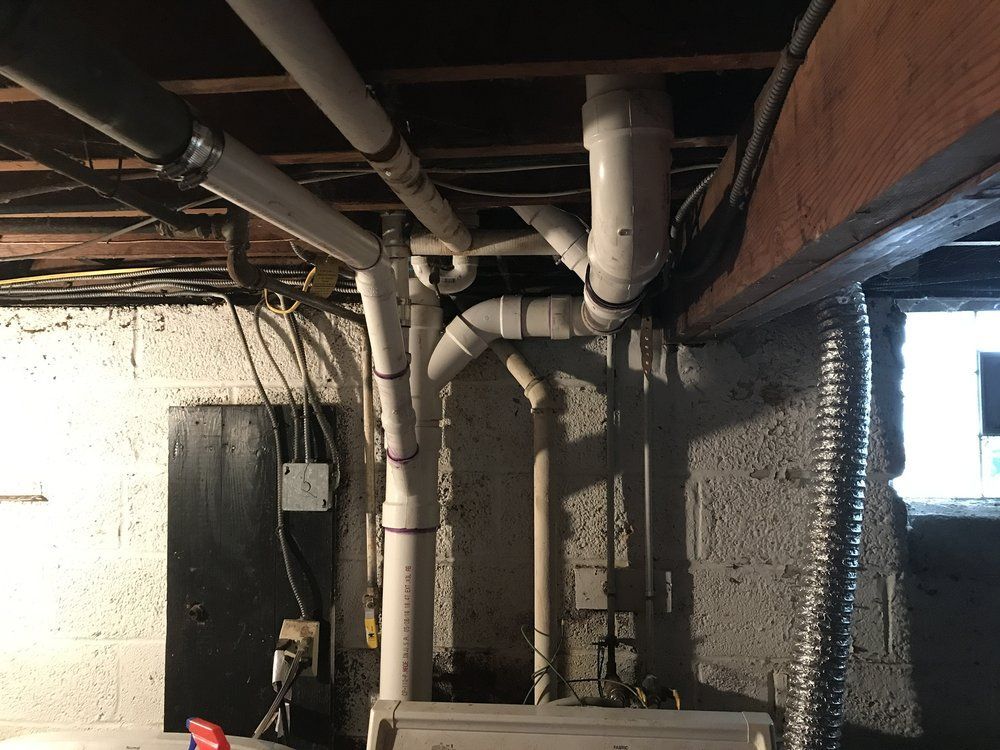 Plumbing pipes against a concrete wall, with a furnace at the bottom and wooden beams above.