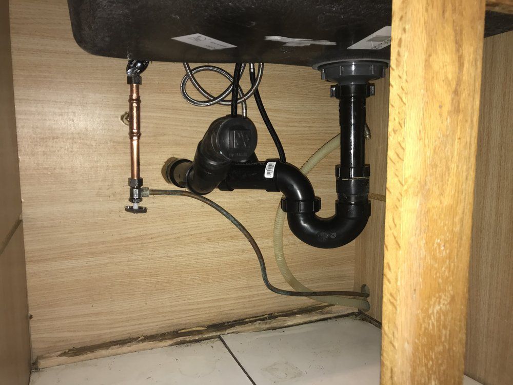 Under-sink plumbing: black drainpipe, copper water pipe, wood cabinet.