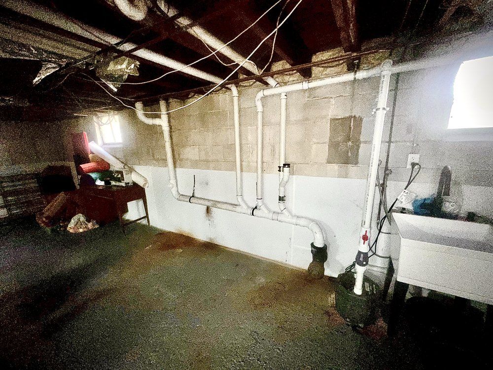 Basement with exposed pipes, concrete walls, and a utility sink. The floor is stained.