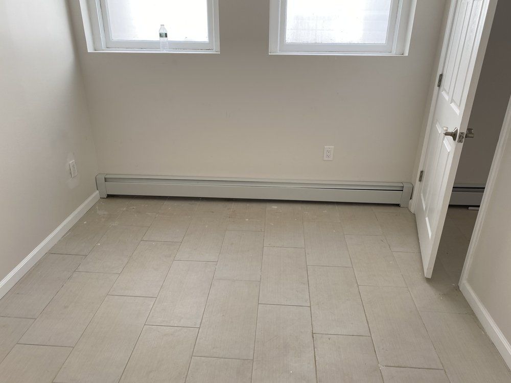 Empty room with beige tiled floor, two windows, and a white door.
